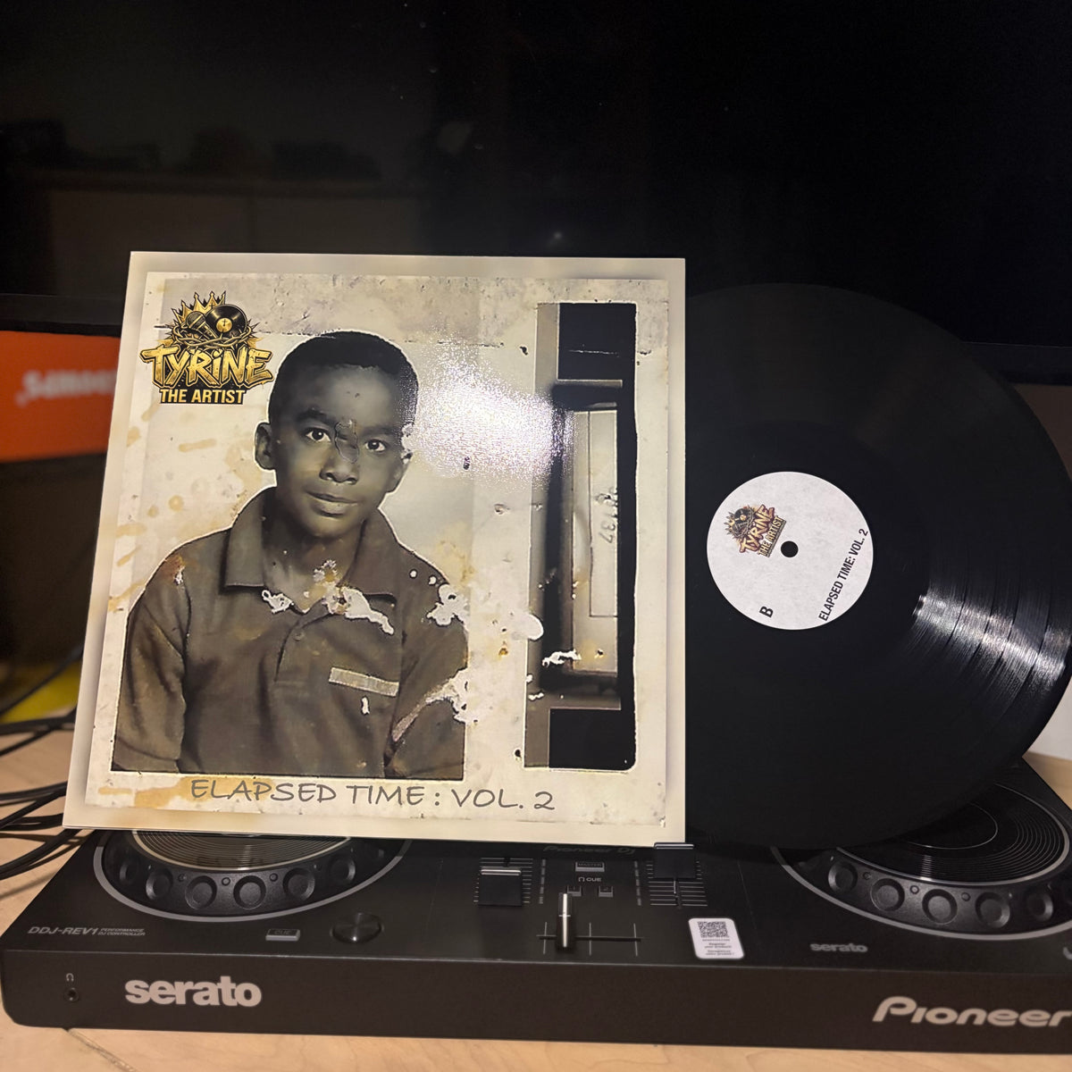 A vinyl record partially pulled from its sleeve, displayed on top of a Pioneer DJ controller. The sleeve features a portrait of a young boy and the text 'Tyrine - The Artist - Elapsed Time: Vol.