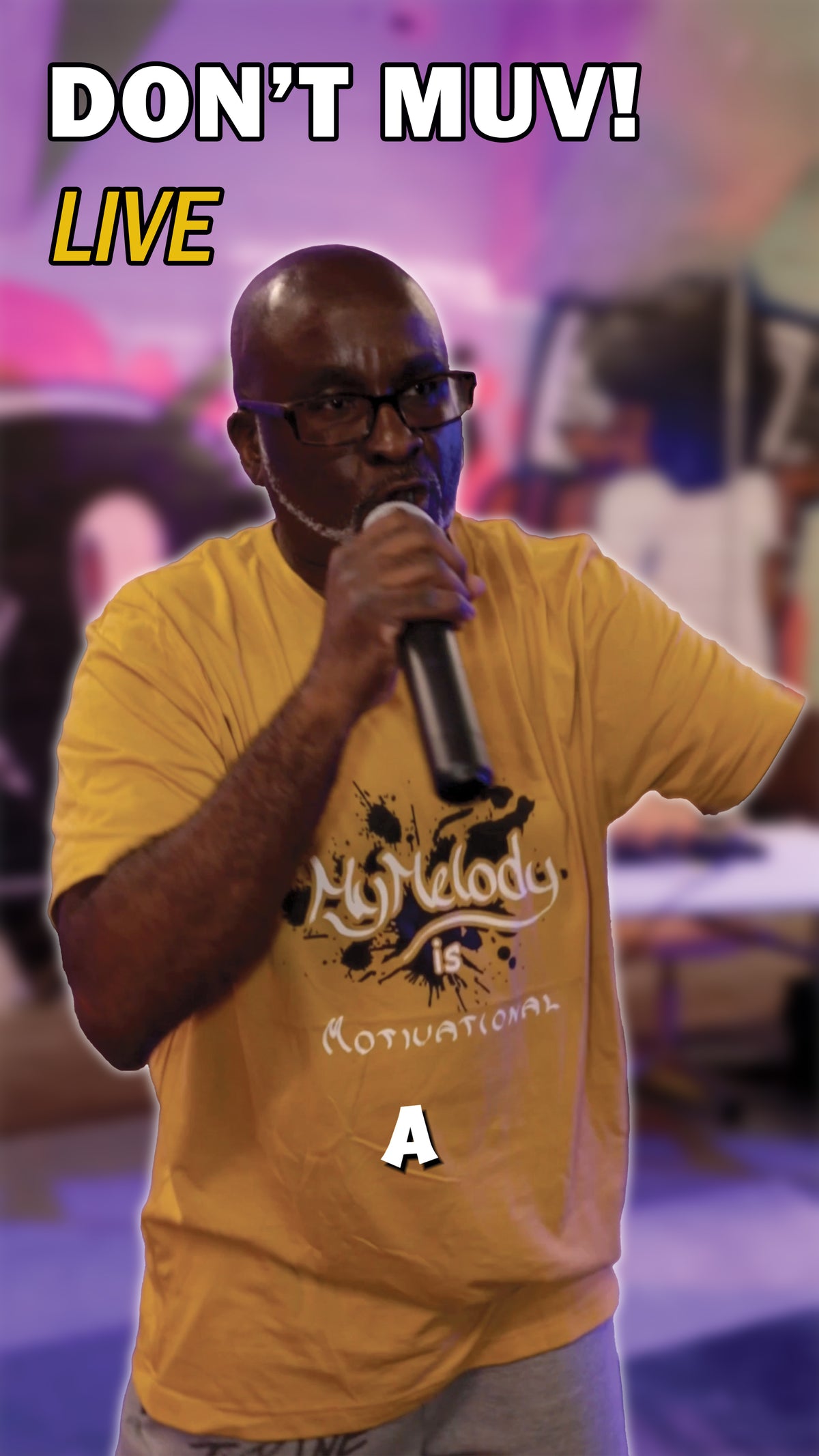 Tyrine the Artist performing Don't Muv! live, holding a microphone and wearing a yellow My Melody Is Motivational shirt.